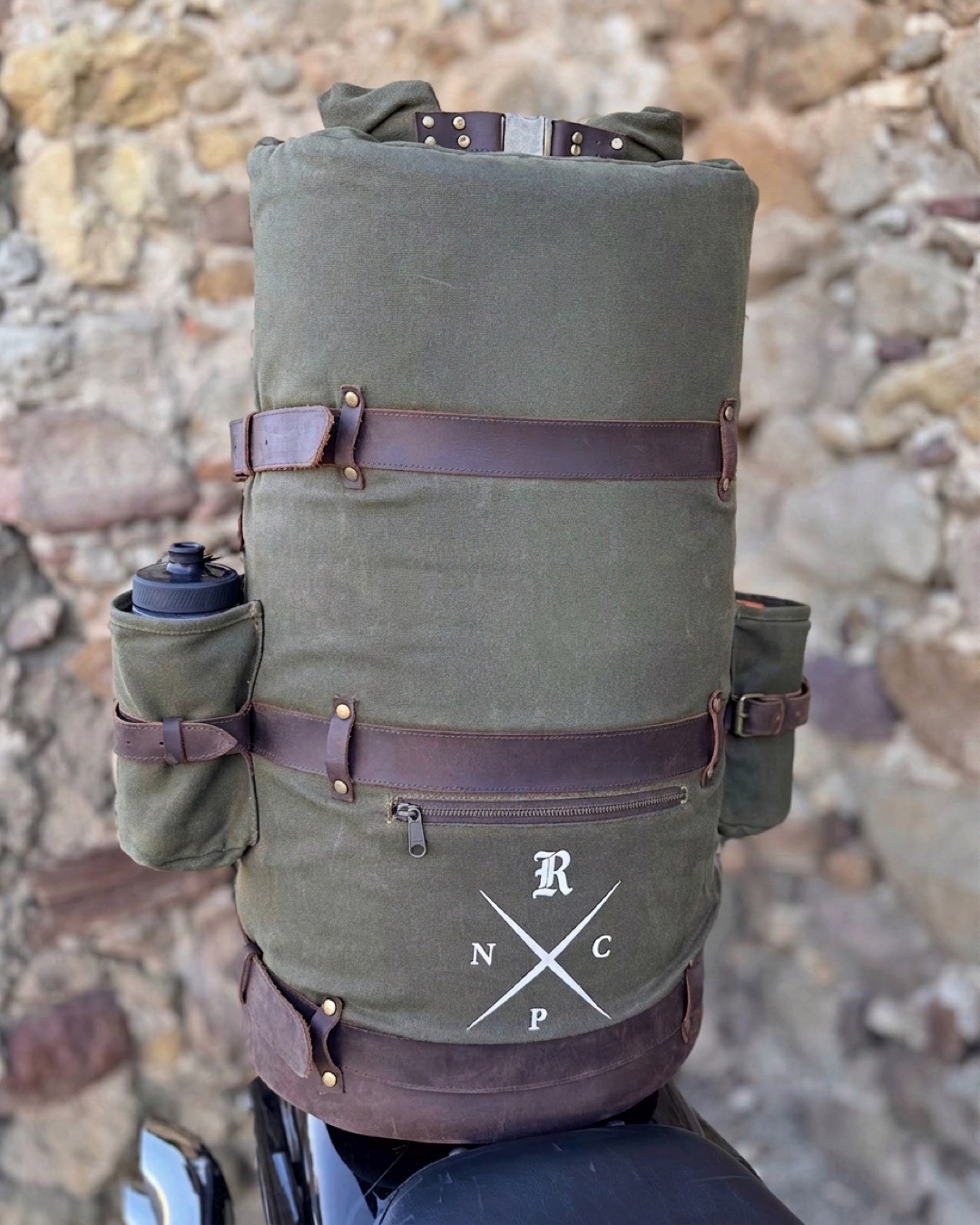 The duffle bag upright on the sissy bar against a stone wall, both bottle holders and the Rebel NPC cross in view